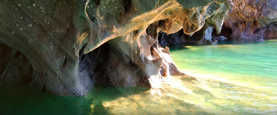 Interior de una caverna de mármol con luz dorada y agua turquesa