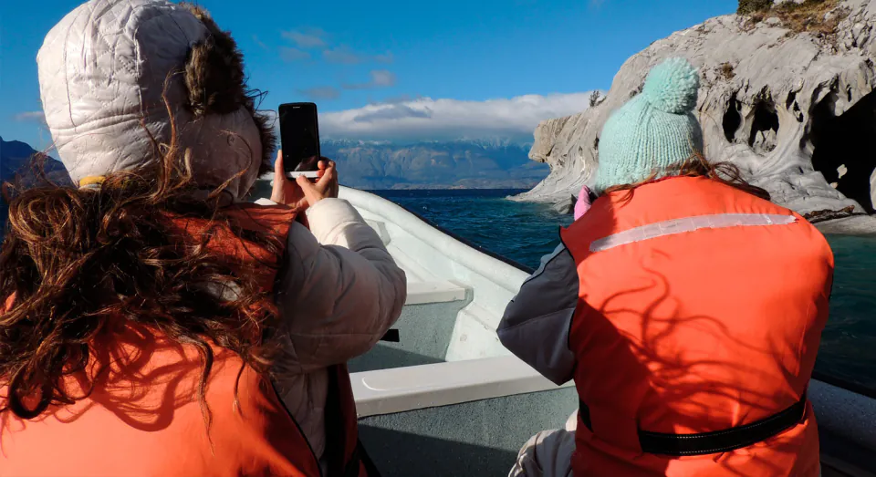Pasajeras con chaleco salvavidas fotografiando las cavernas desde la lancha